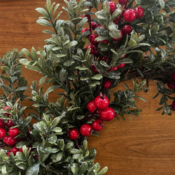 Frosted green foliage garland with bright red berries arranged on a warm brown wooden surface.