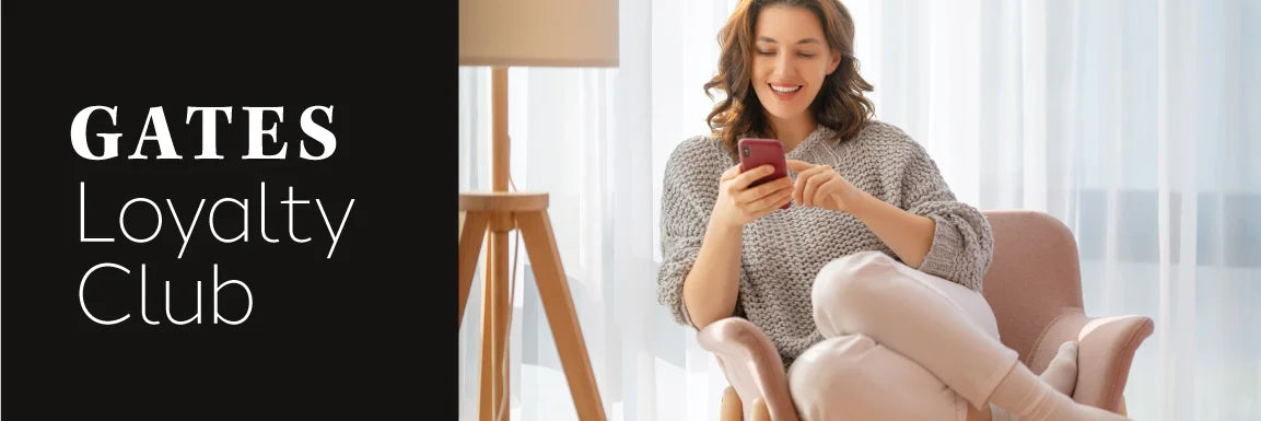 Promotional banner for the Gates Loyalty Club featuring a woman sitting in a pink armchair on a white sofa, smiling while looking at her phone. On the left is a black vertical panel with the text 'GATES Loyalty Club' in white.