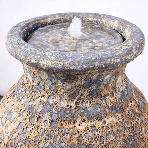 A close-up of the Altico rustic grey water feature with a textured, porous surface and a small flow of water from its central saucer.