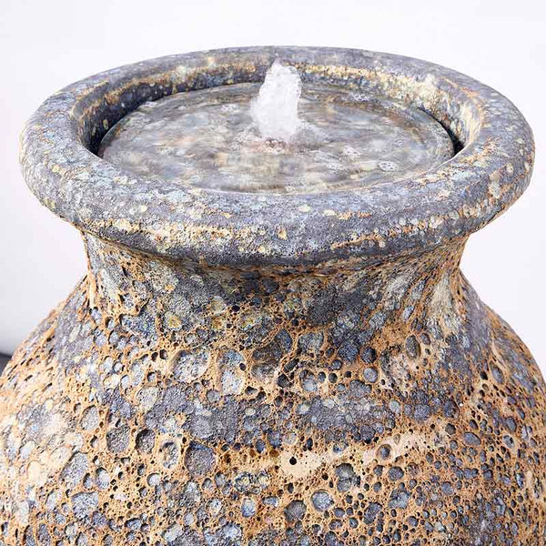 A close-up of the Altico rustic grey water feature with a textured, porous surface and a small flow of water from its central saucer.