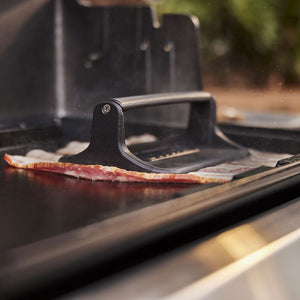 Weber Griddle Press in use, flattening bacon on a griddle