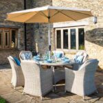 Bramblecrest Monterey Sandstone 6 Seat Elliptical Dining Set with Parasol & Base in the garden