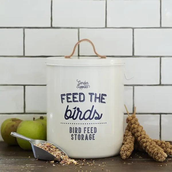 A Burgon & Ball 'Feed the Birds' Bird Food Tin sat on a kitchen counter with a scoop of feed. The tin is white stone coloured with blue typography.