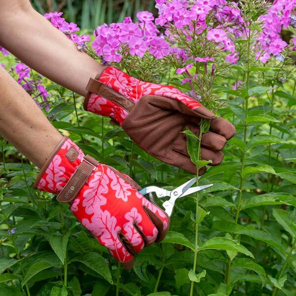 Hands wearing the Red Oak patterned Burgon & Ball Gardening Gloves to prune plants.