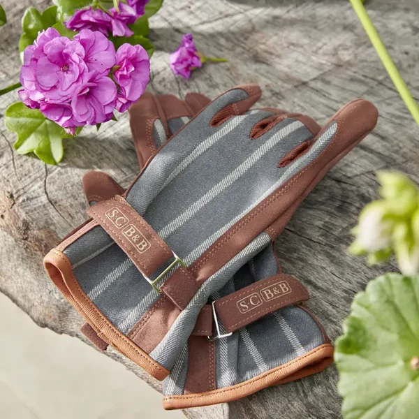 A pair of Burgon & Ball Sophie Conran Everyday Gloves sat outside on a wooden log surface.