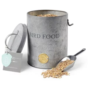 A Burgon & Ball Sophie Conran Galvanized Bird Food Tin. The lid is off and the tin is filled with seed. The scoop is also full and lying in front.