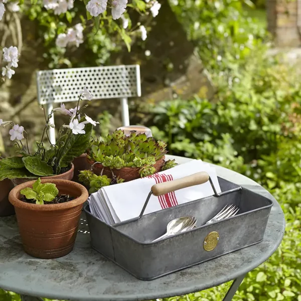 A metal Burgon & Ball Sophie Conran Galvanized Trug on a patio table holding cutlery and napkins.
