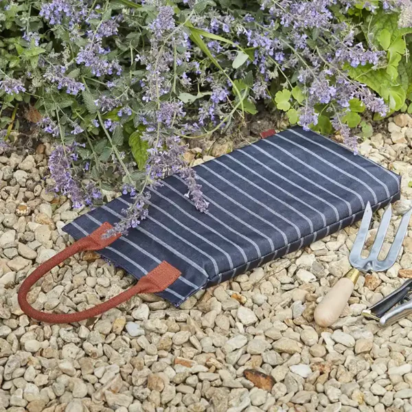 The navy and white striped Burgon & Ball Sophie Conran Garden Kneeler pad with brown handle, sat flat on gravel.