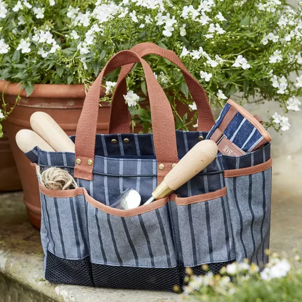 The blue Burgon & Ball Sophie Conran Tool Bag sat on the ground outside , holding a range of common gardening tools that can be seen sticking out.