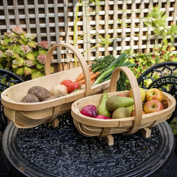 The medium and large Burgon & Ball Traditional Wooden Trugs on an outdoor bistro table, both containing homegrown produce.