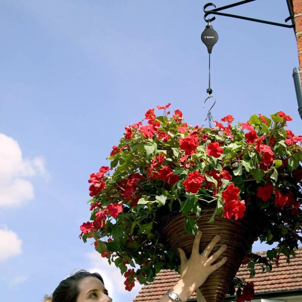 The Darlac Hi-Lo Pulley, suspending a hanging basket. A woman is lifting up the hanging basket to the required height on the pulley.