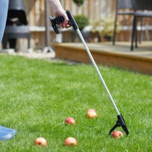 A hand holding the EasyPicker to collect an apple off the grass. The gripper end is clasping round the apple and the trigger is pulled.