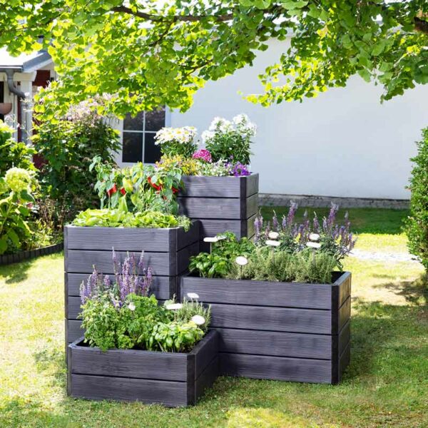 An assortment of different size and height stacks of Ergo Quadro Raised Beds. The black wood-effect beds are full of plants.