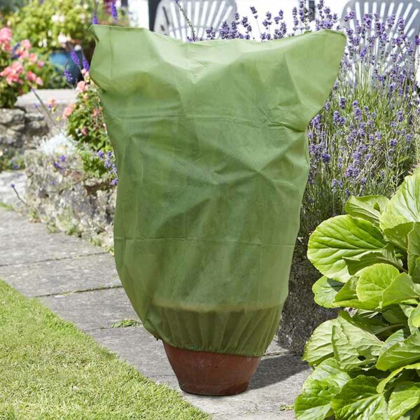 A green G30 Plant Warming Fleece Cover over a terracotta potted plant outside on a garden path.