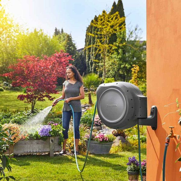 A woman watering using the hose from the GARDENA Wall-Mounted RollUp Hose Box.