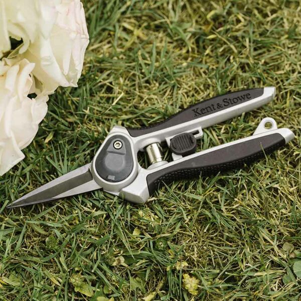 A pair of Kent & Stowe Eversharp Garden Snips lying on the grass. The snips have black rubber handles and dark carbon blades.