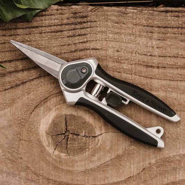 A pair of Kent & Stowe Eversharp Garden Snips placed on a log. The snips have black rubber handles and dark carbon blades.