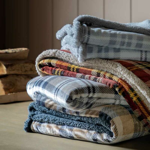 A pile of blankets with the Kilburn & Scott Tartan Sherpa Throw in Natural