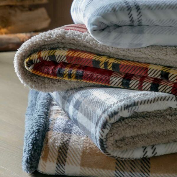 A pile of different blankets including the Kilburn & Scott Tartan Sherpa Throw in Natural