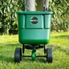 A green Miracle-Gro rotary lawn spreader being pushed forward on grass.