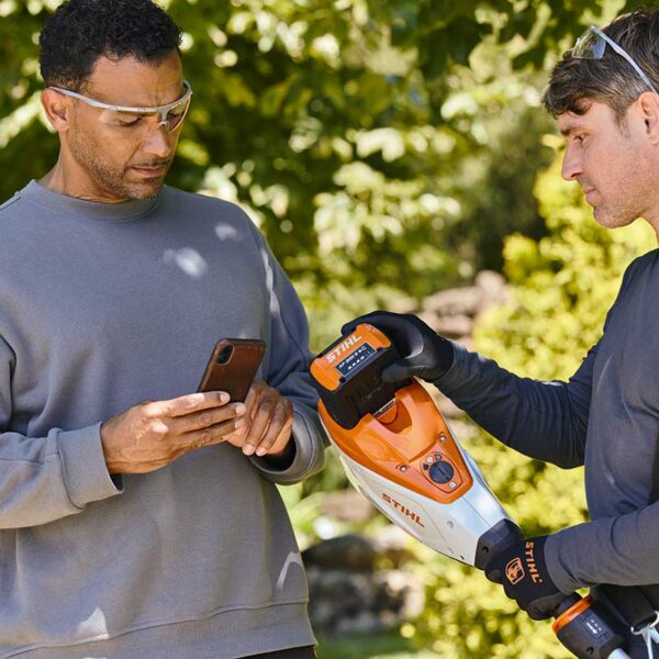 A man standing with the STIHL AP 300 S Battery, connecting it to his phone.