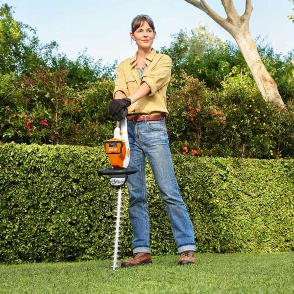 A woman posing with the STIHL HSA 50 Cordless Hedge Trimmer resting against the ground.