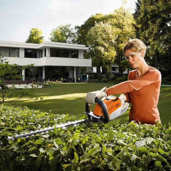 A woman trimming a hedge using the STIHL HSA 66 Cordless Hedge Trimmer.