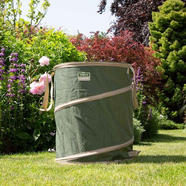 A large green and cream trimmed pop-up gardening tidy bag for collecting garden waste., sat outside on a lawn. It has cream handles and a spring that provides the shape.