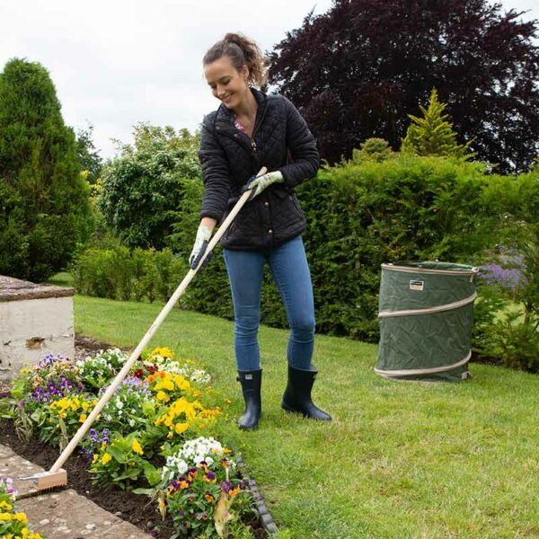 A woman cleaning a patio using the Town & Country Pop-Up Garden Tidy Bag to collect the waste.