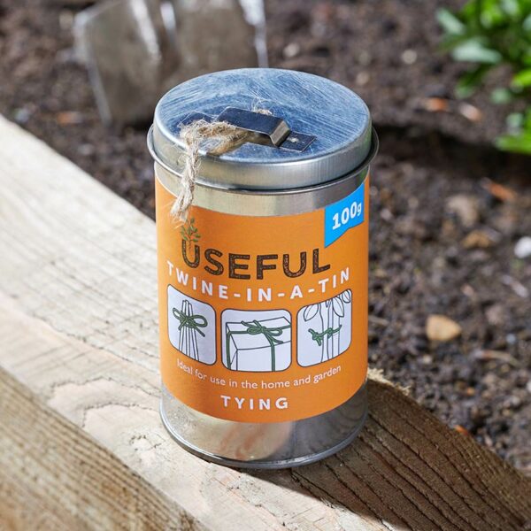 A small 100g tin of gardening twine, sat outside on a wooden sleeper.