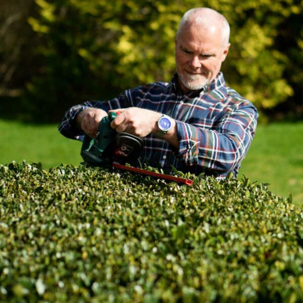 A man using the Webb Classic 500W 51cm (20") Hedge Trimmer to cut the flat top of a hedge.